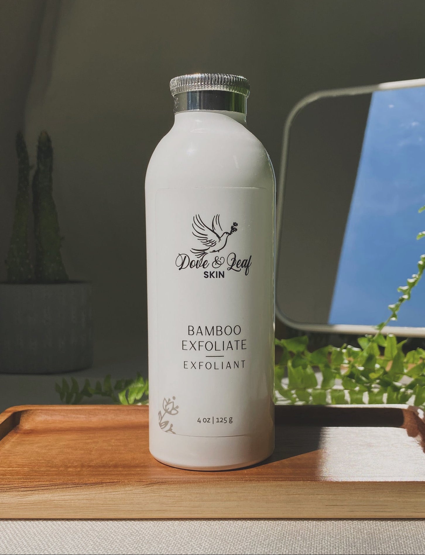 White skincare bottle labeled 'Dove & Leaf' on a wooden tray with plants in the background