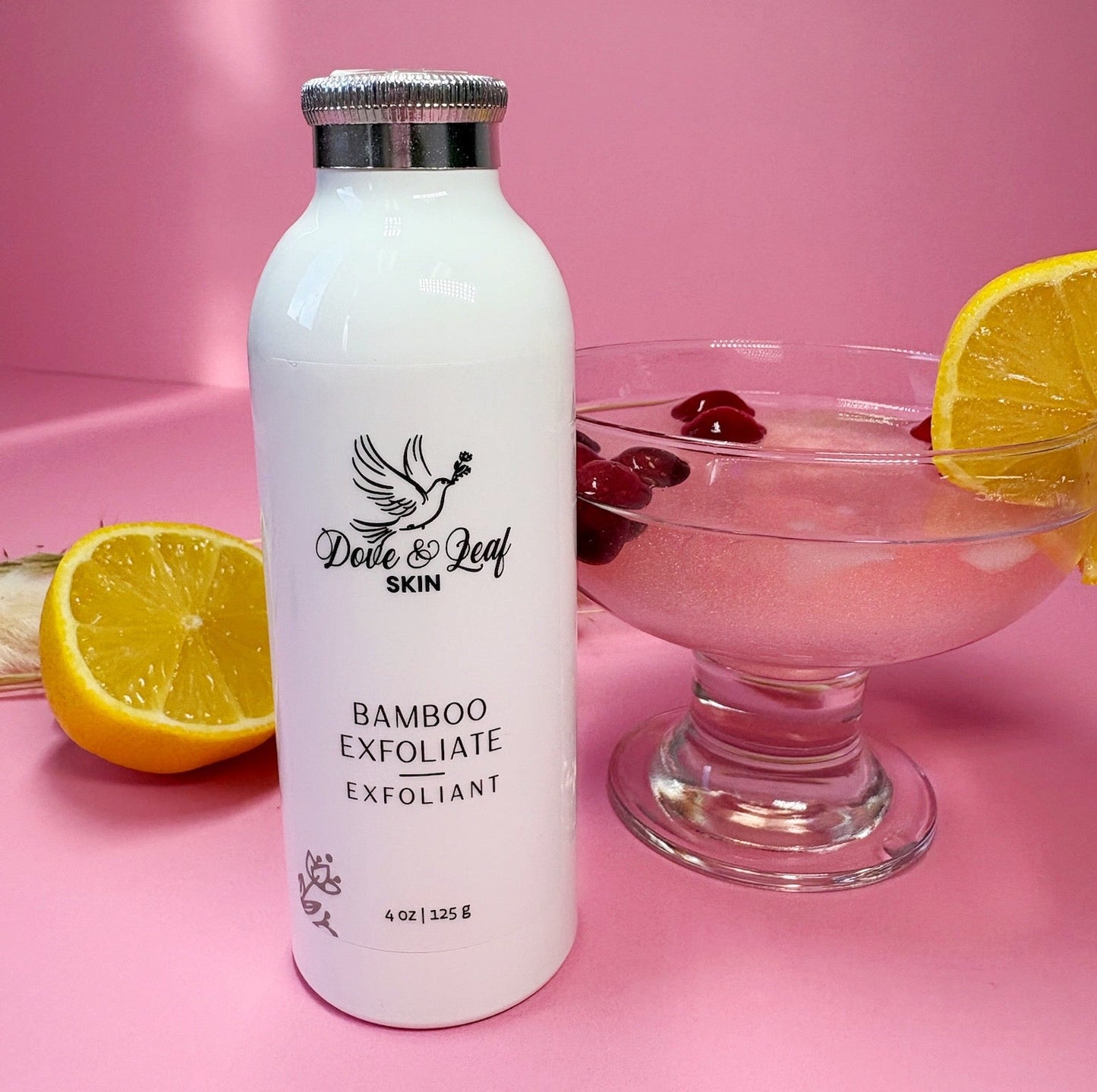 White bottle labeled 'Dove & Leaf Skin' on a pink background with a glass of pink drink and lemon slices.
