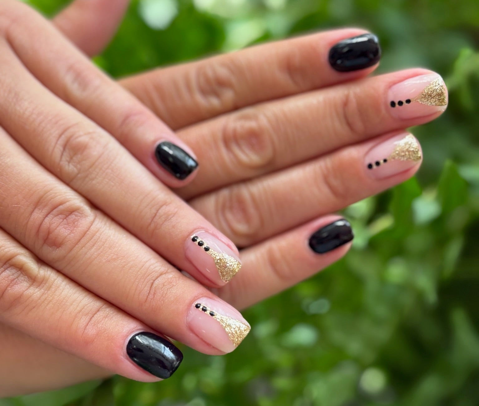 Hand with black and gold nail polish against a green leafy background