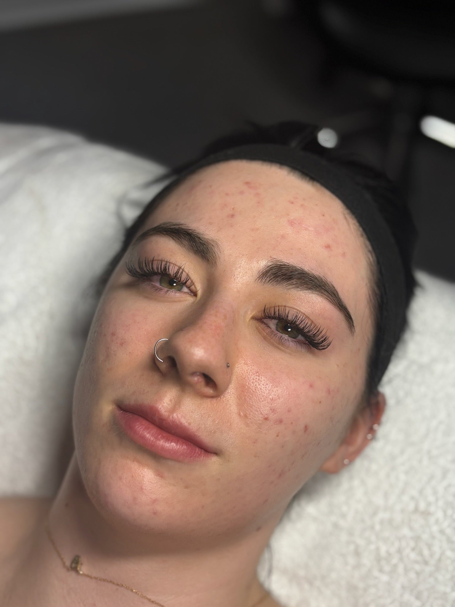 Woman lying down with a black headband on, showing her face with lash extensions.
