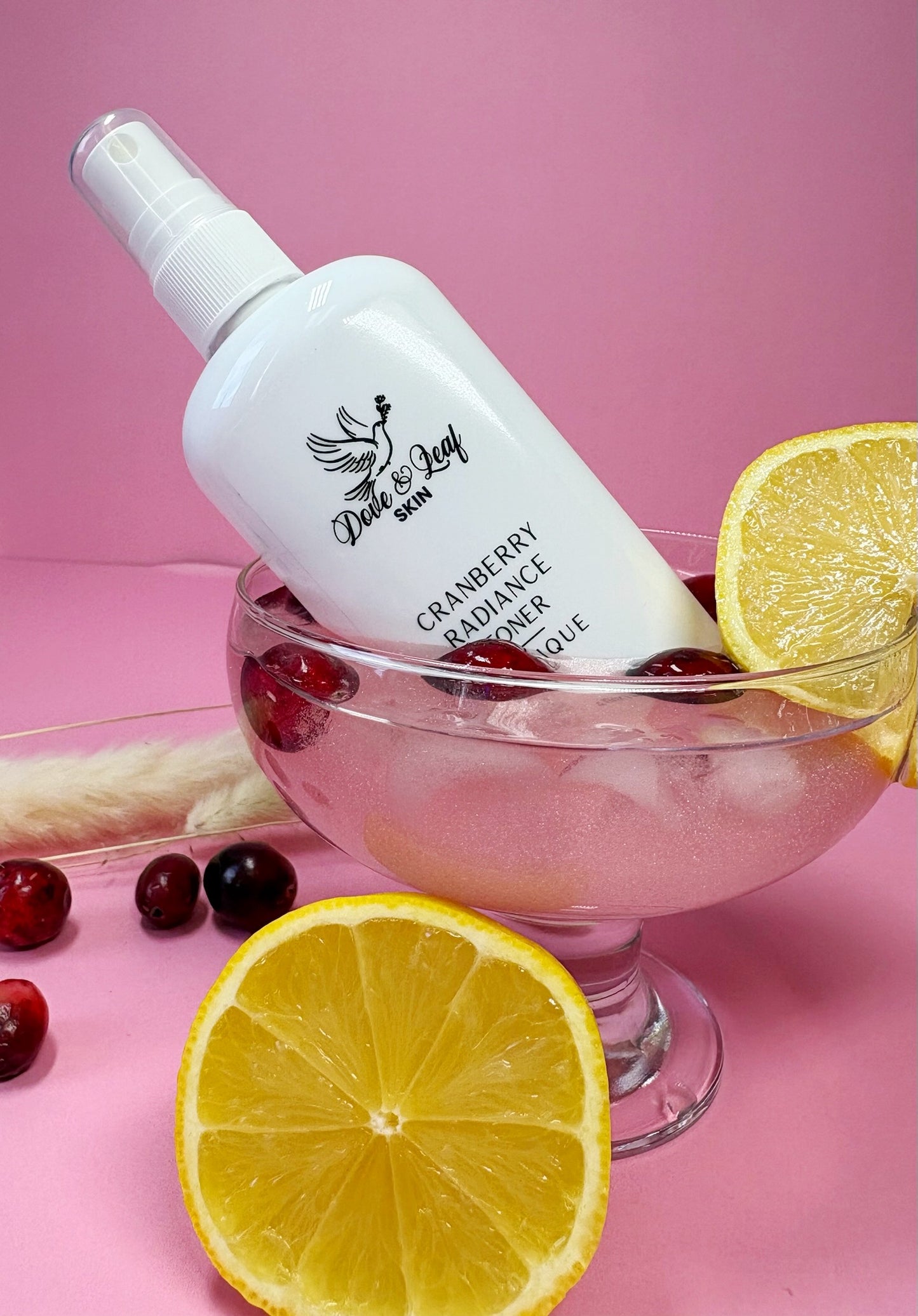 White bottle labeled 'Dote & Leaf' with cranberries and lemons on a pink background