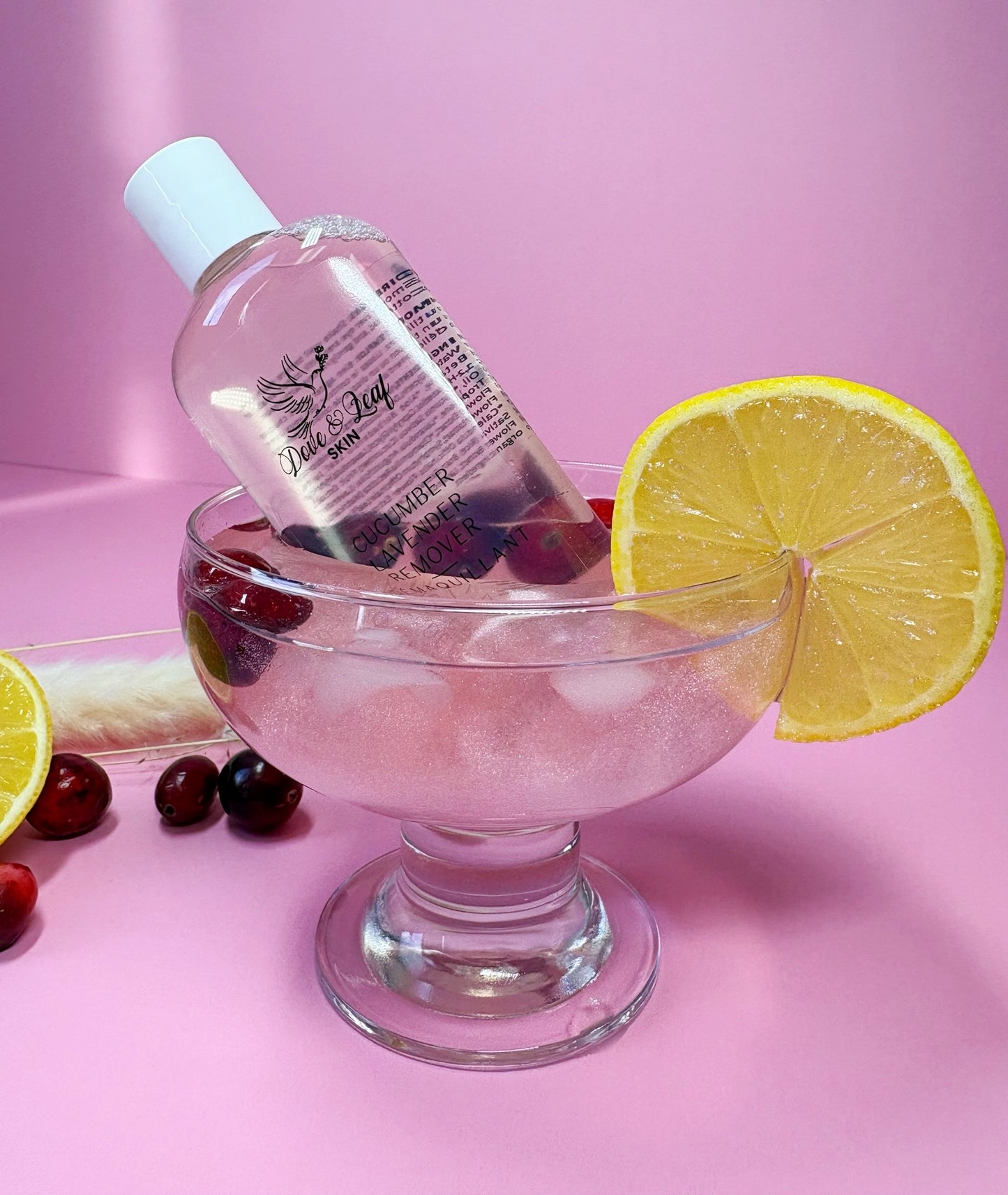 Bottle of pink liquid with a lemon slice on a pink background