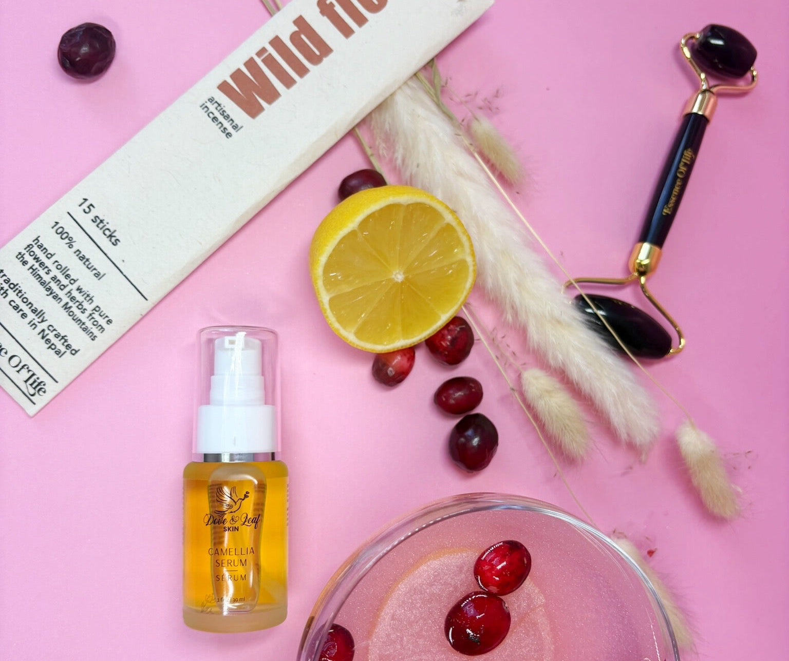 Wild Flora product with a lemon, cherries, and a roller on a pink background