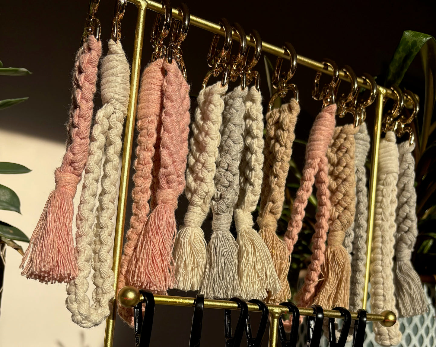 Set of macrame keychains in various colors hanging on a gold rack.