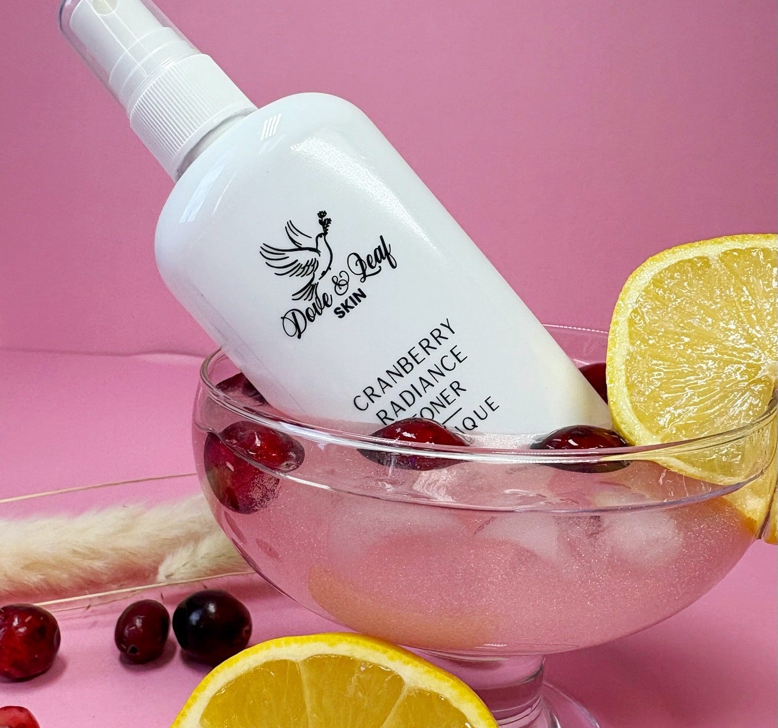 White bottle labeled 'Dove & Leaf' with cranberries and lemons on a pink background