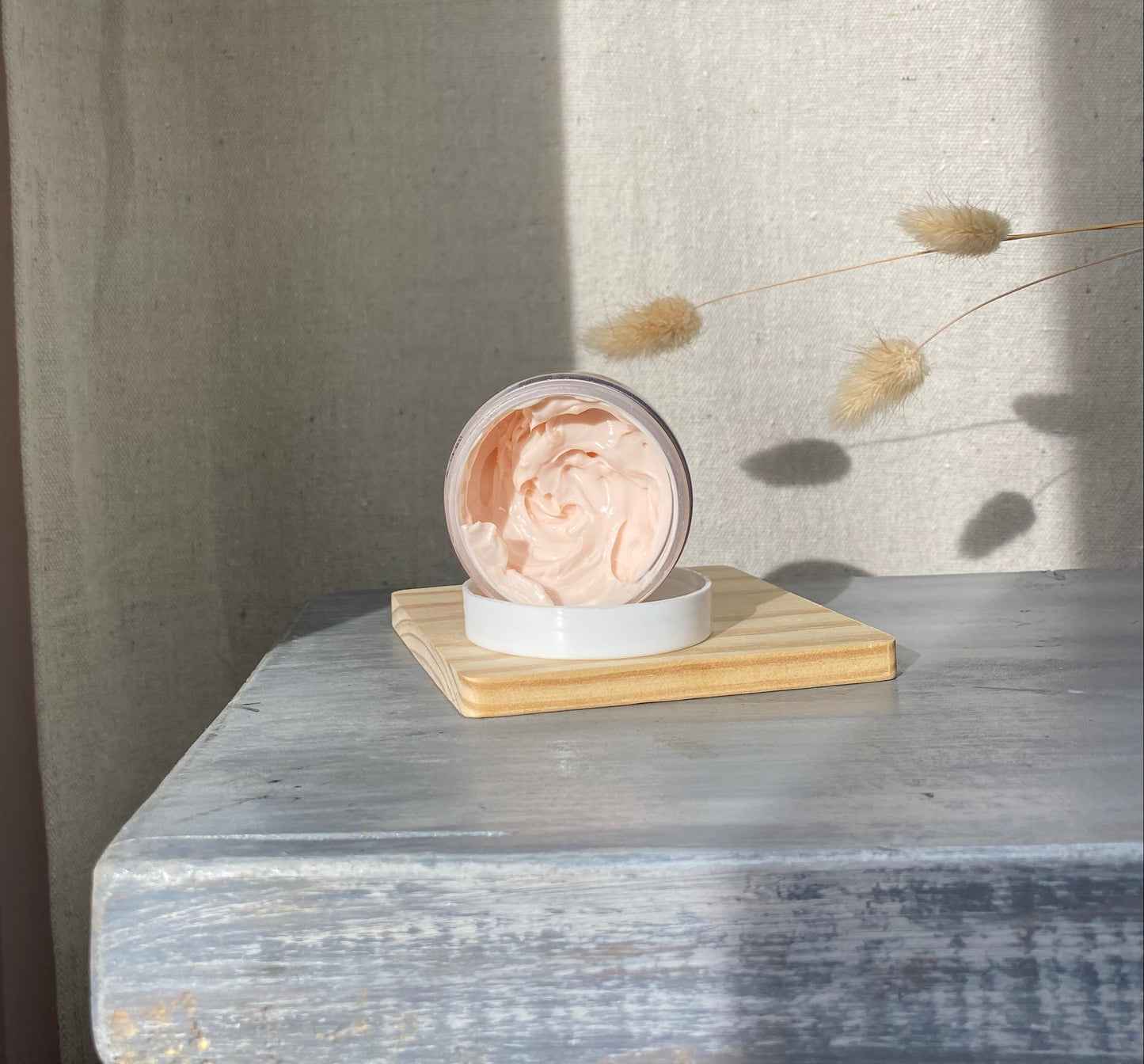 Small round container with a lid on a textured surface, pink facial cream
