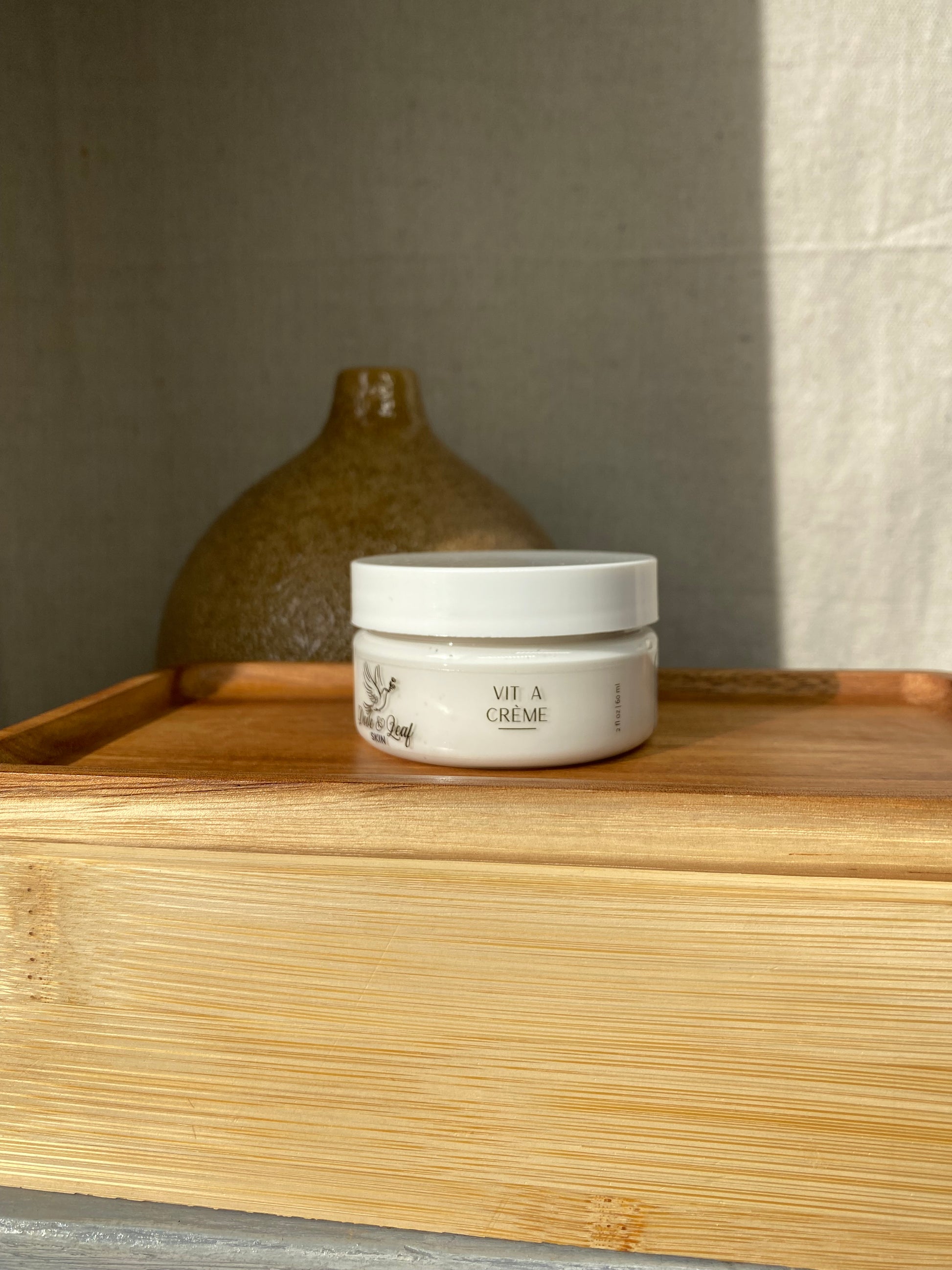 Small container of cream on a wooden surface next to a ceramic jar.