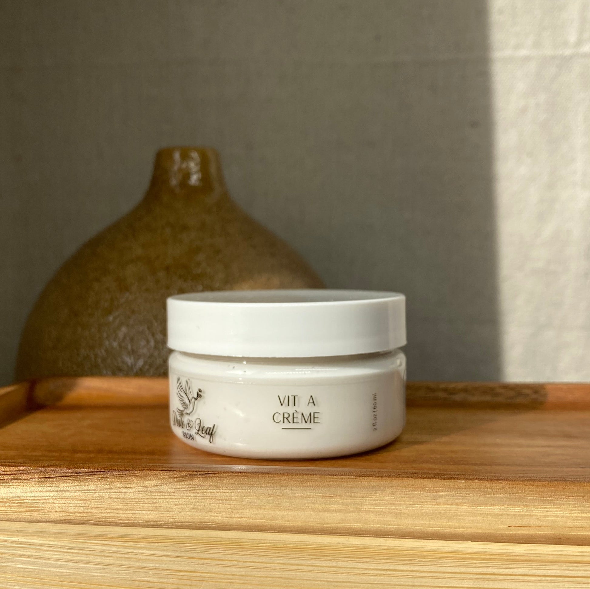 Small container of cream on a wooden surface next to a ceramic jar.